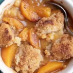 Freshly baked Southern peach cobbler in a white baking dish with golden crust and juicy peach filling